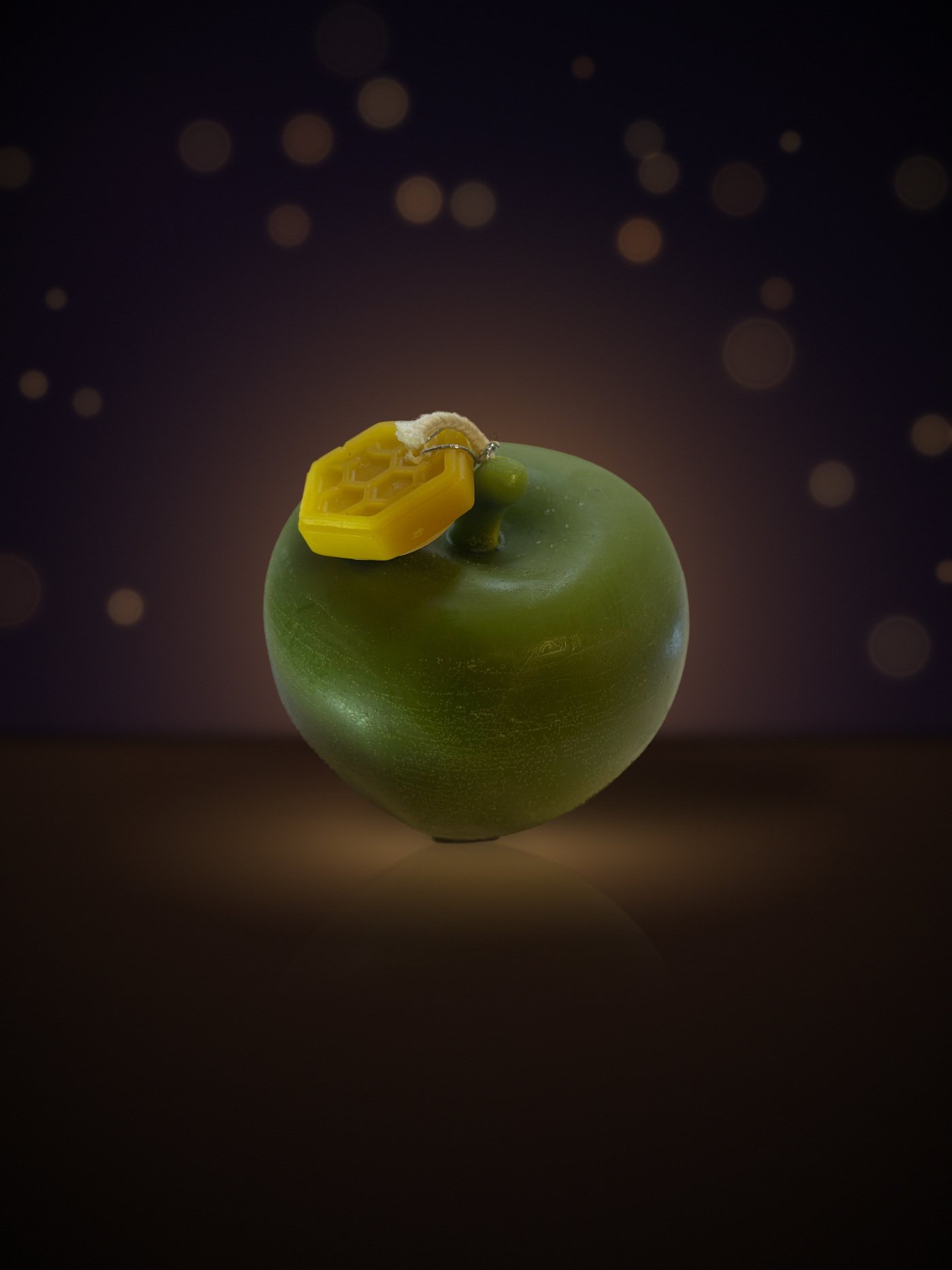 Maine beeswax apple candle in green with honeycomb tag, warm candlelit background