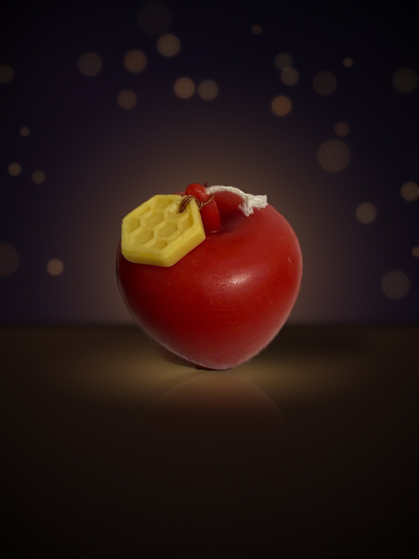 Maine beeswax red apple candle seen from above with honeycomb tag, warm candlelit background