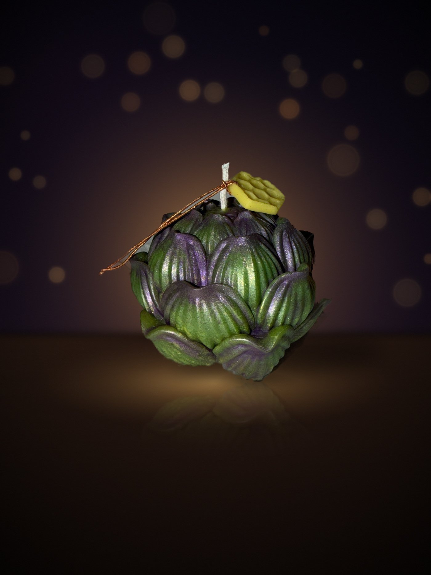 Maine beeswax artichoke candle, side view, forest green with purple mica and honeycomb tag, warm candlelit background