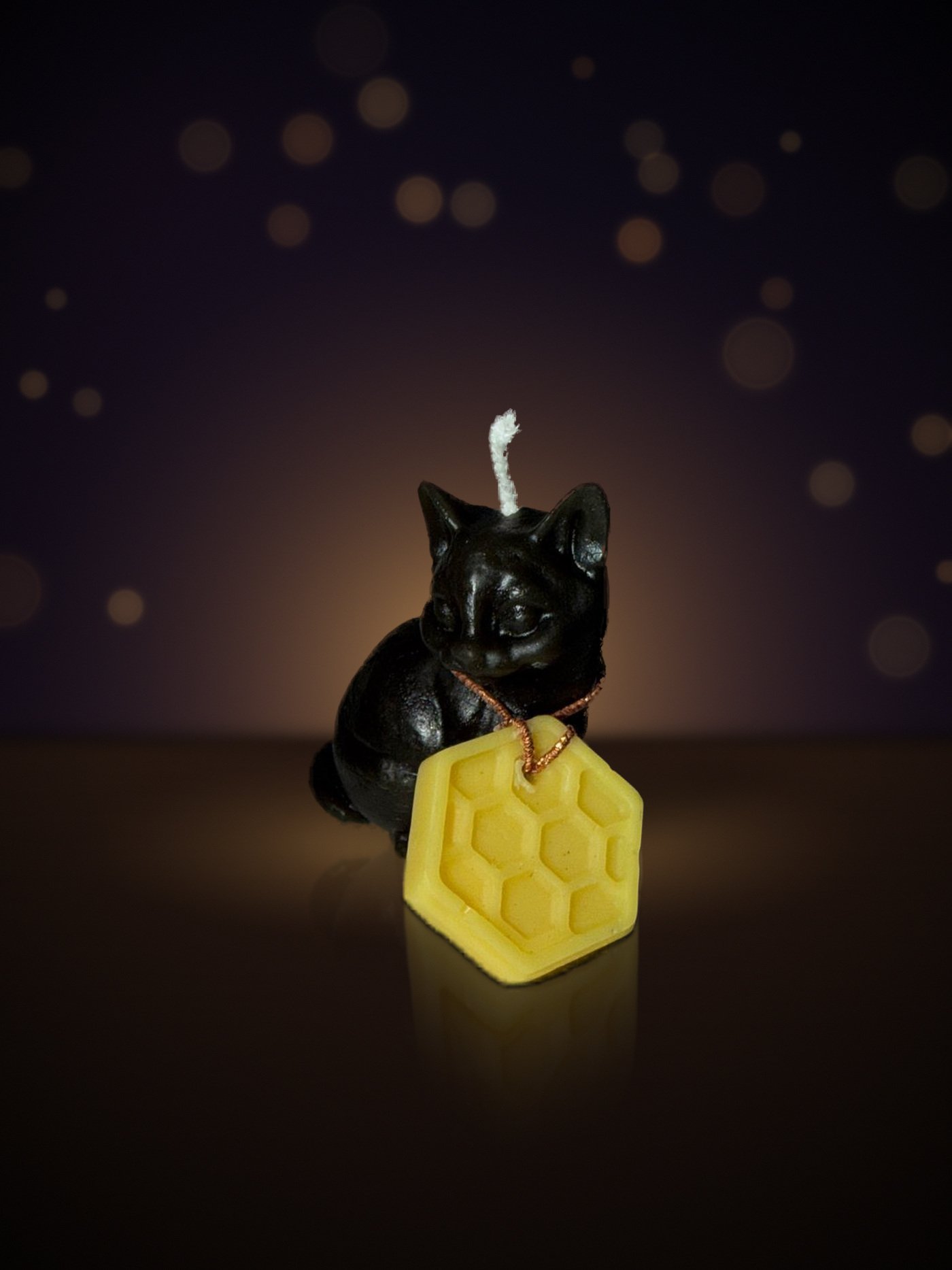 Maine beeswax sitting kitten candle in matte black with honeycomb tag, warm candlelit background