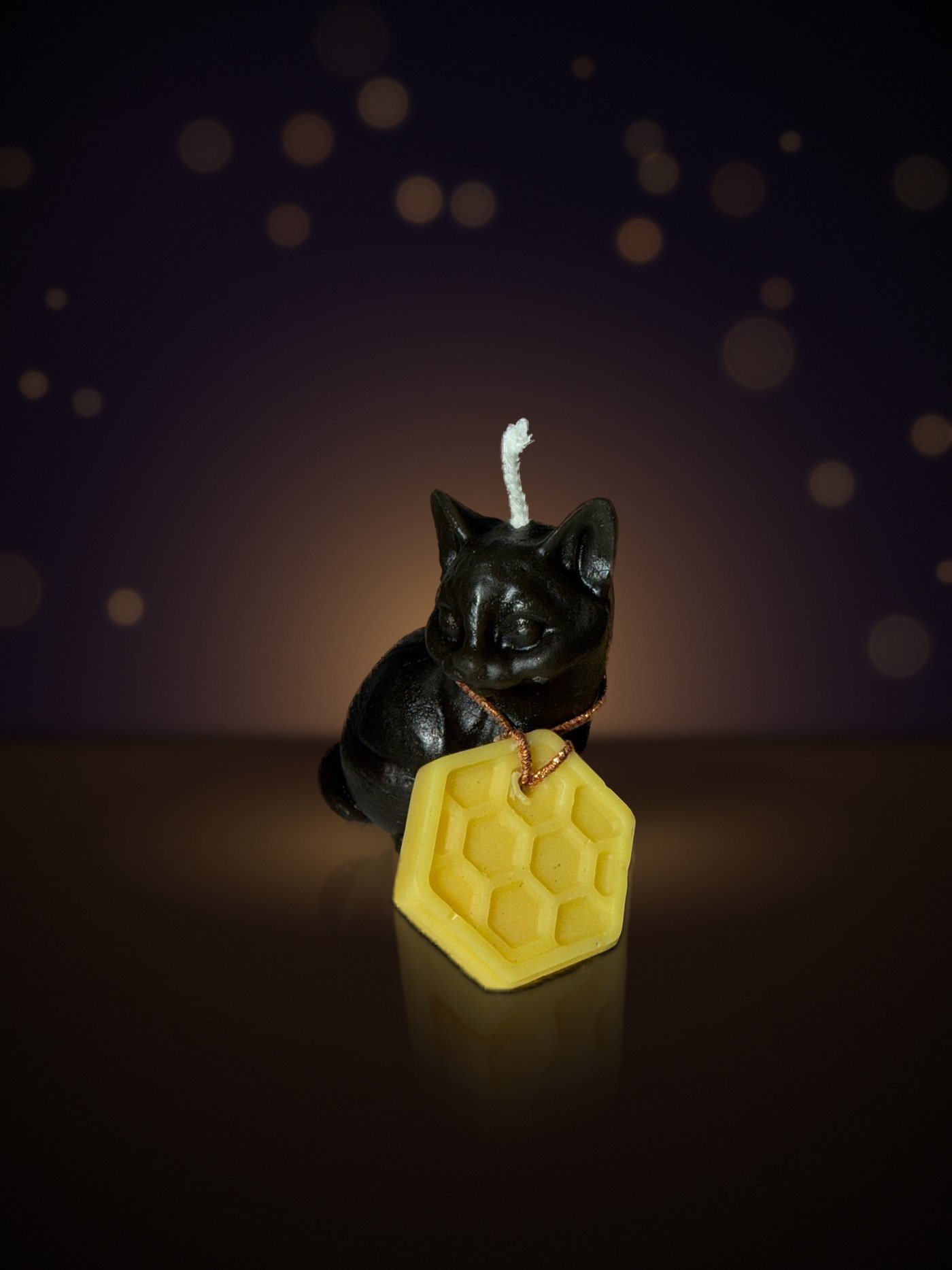 Maine beeswax kitten candle, side view with honeycomb charm, warm candlelit background