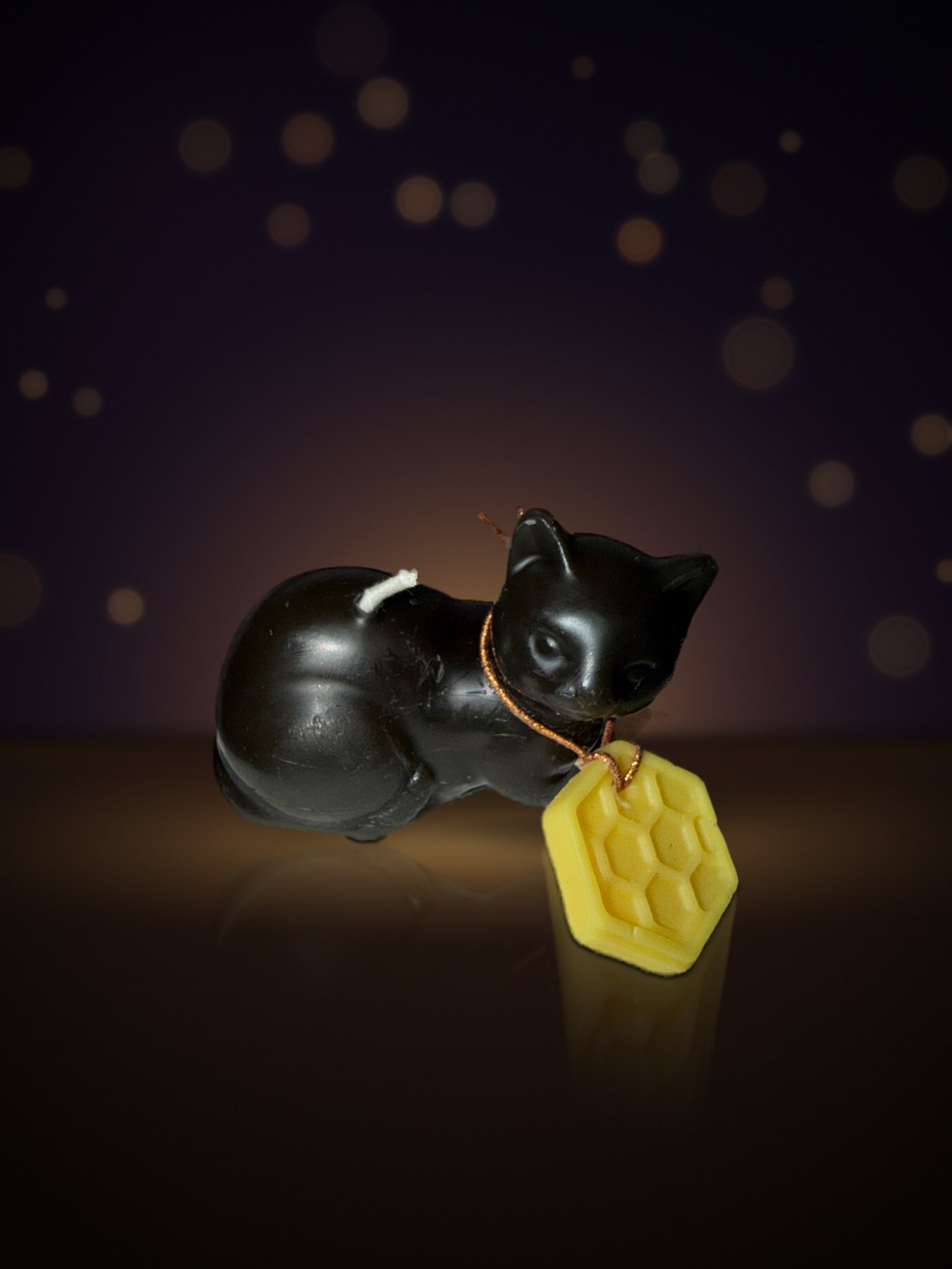 Maine beeswax Meo time cat candle in matte black with honeycomb tag, warm candlelit background