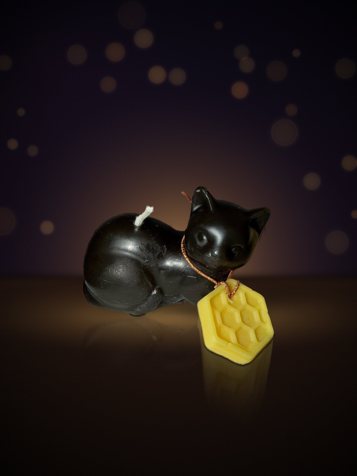 Maine beeswax Meo cat candle, side view with honeycomb charm, warm candlelit background