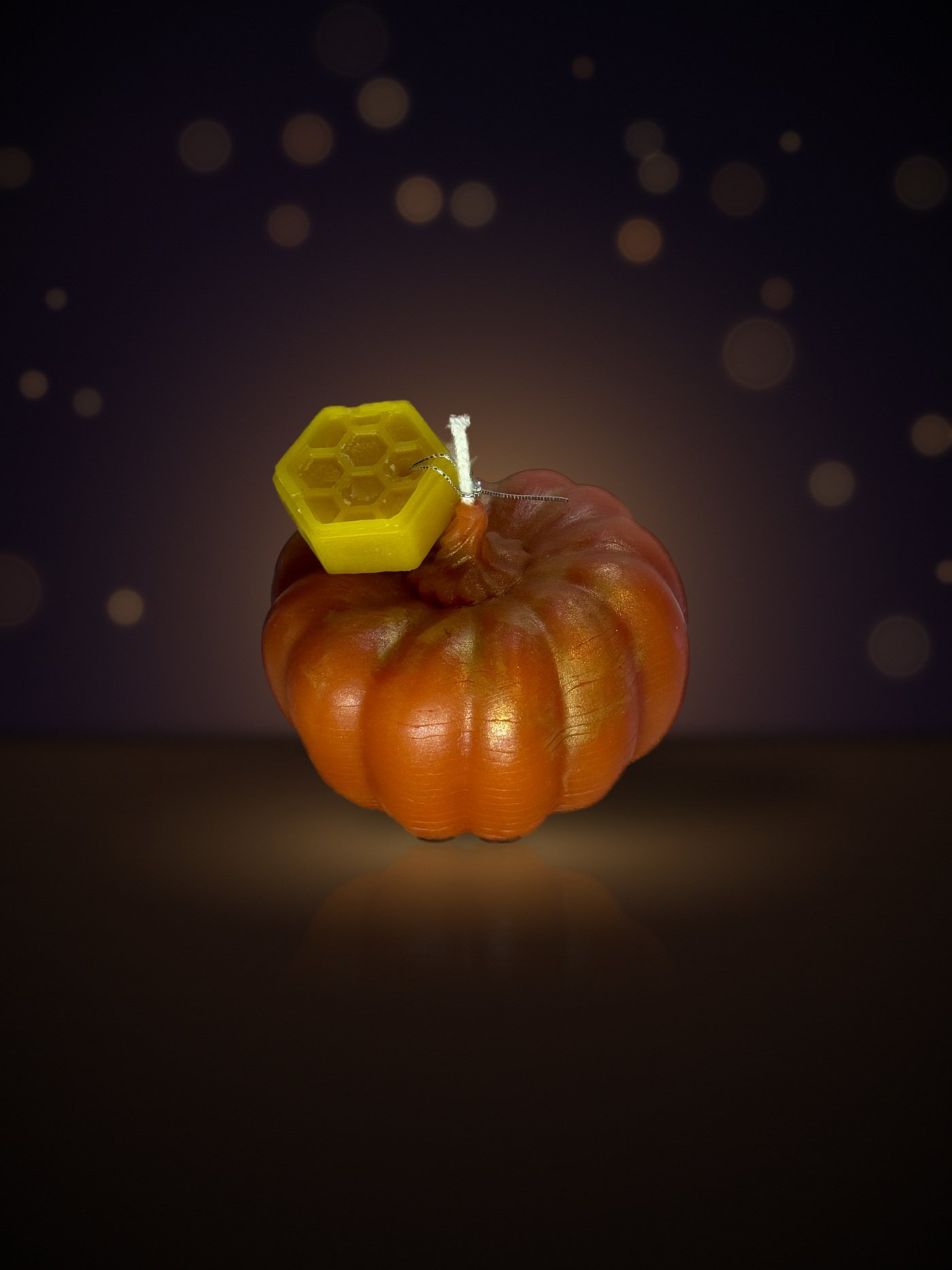 Maine beeswax pumpkin candle, bumpy large shape, orange with gold mica, with honeycomb tag, warm candlelit background