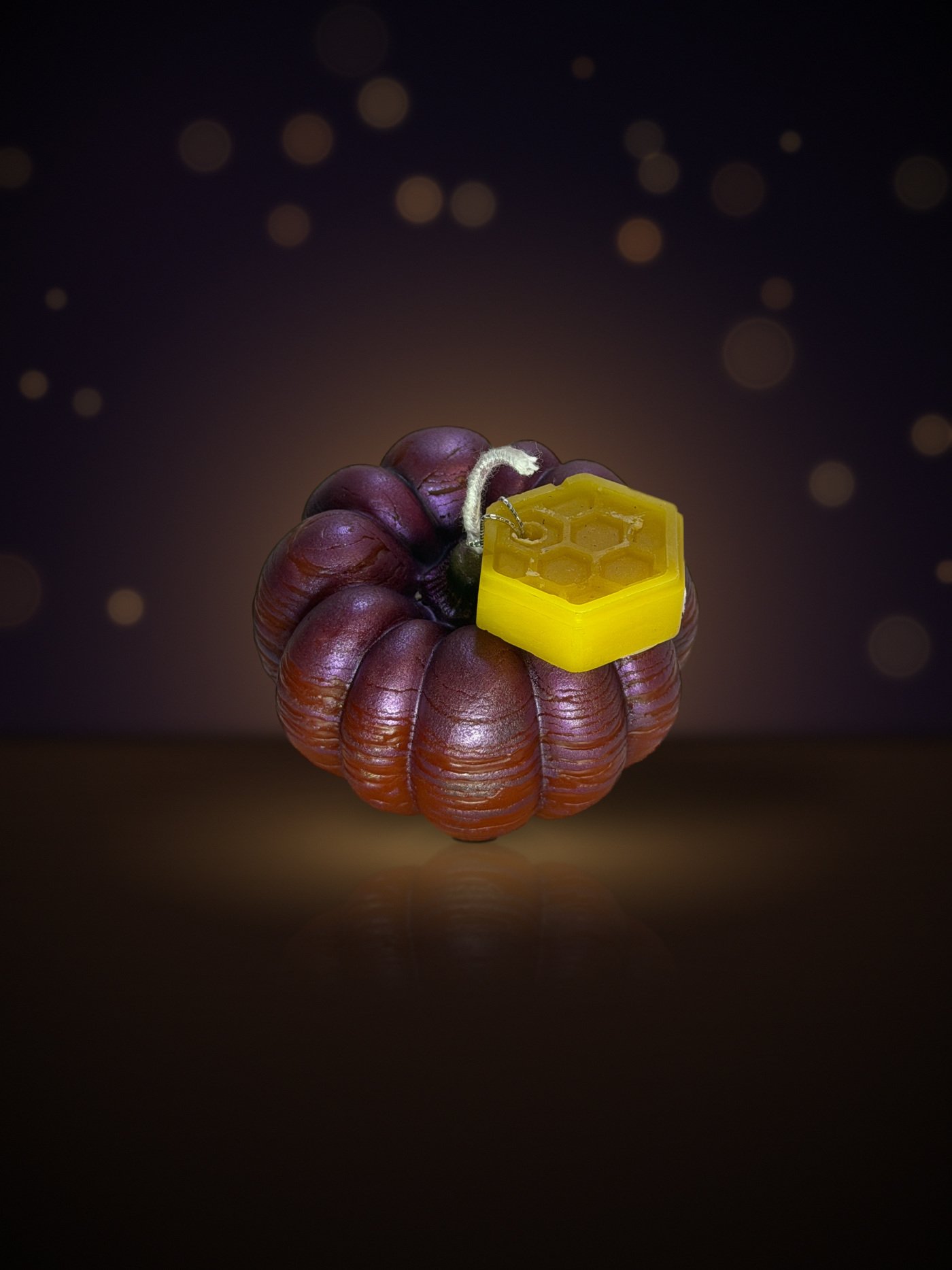 Maine beeswax pumpkin candle, bumpy small shape, purple-red, with honeycomb tag, warm candlelit background