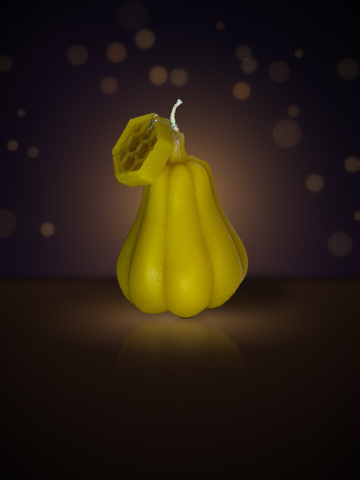 Maine beeswax pumpkin candle, curly stem shape, yellow, with honeycomb tag, warm candlelit background