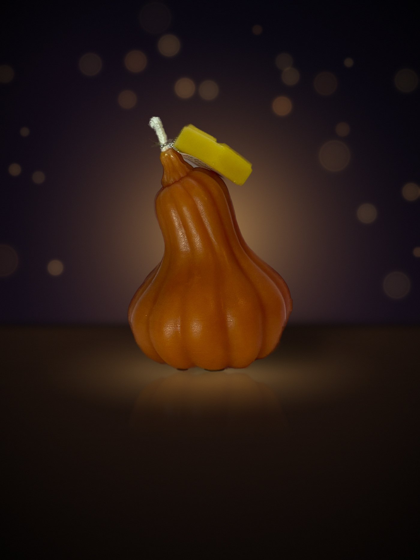 Maine beeswax pumpkin candle, big gourd shape, orange, with honeycomb tag, warm candlelit background