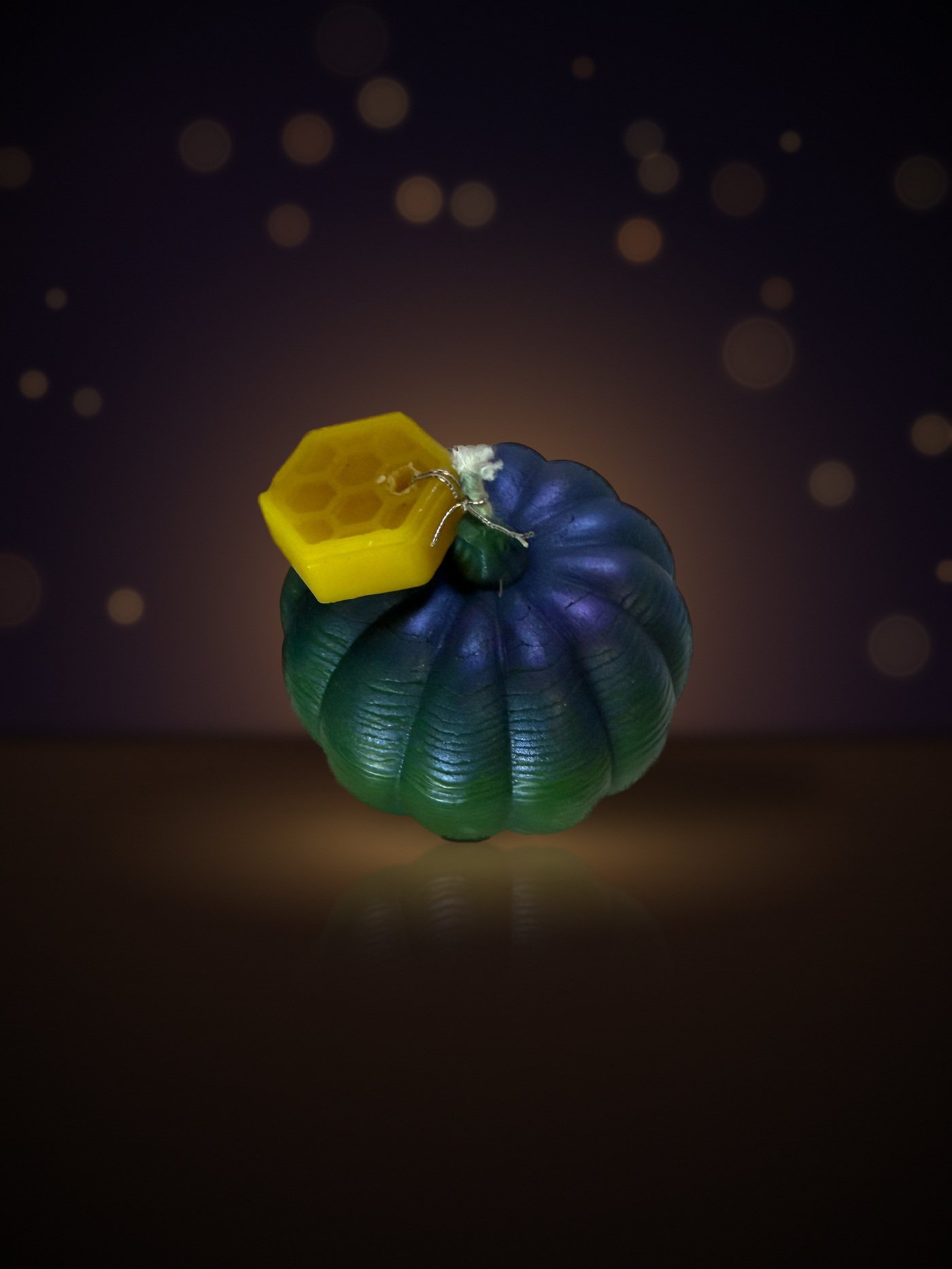 Maine beeswax pumpkin candle, medium shape, blue-green, with honeycomb tag, warm candlelit background