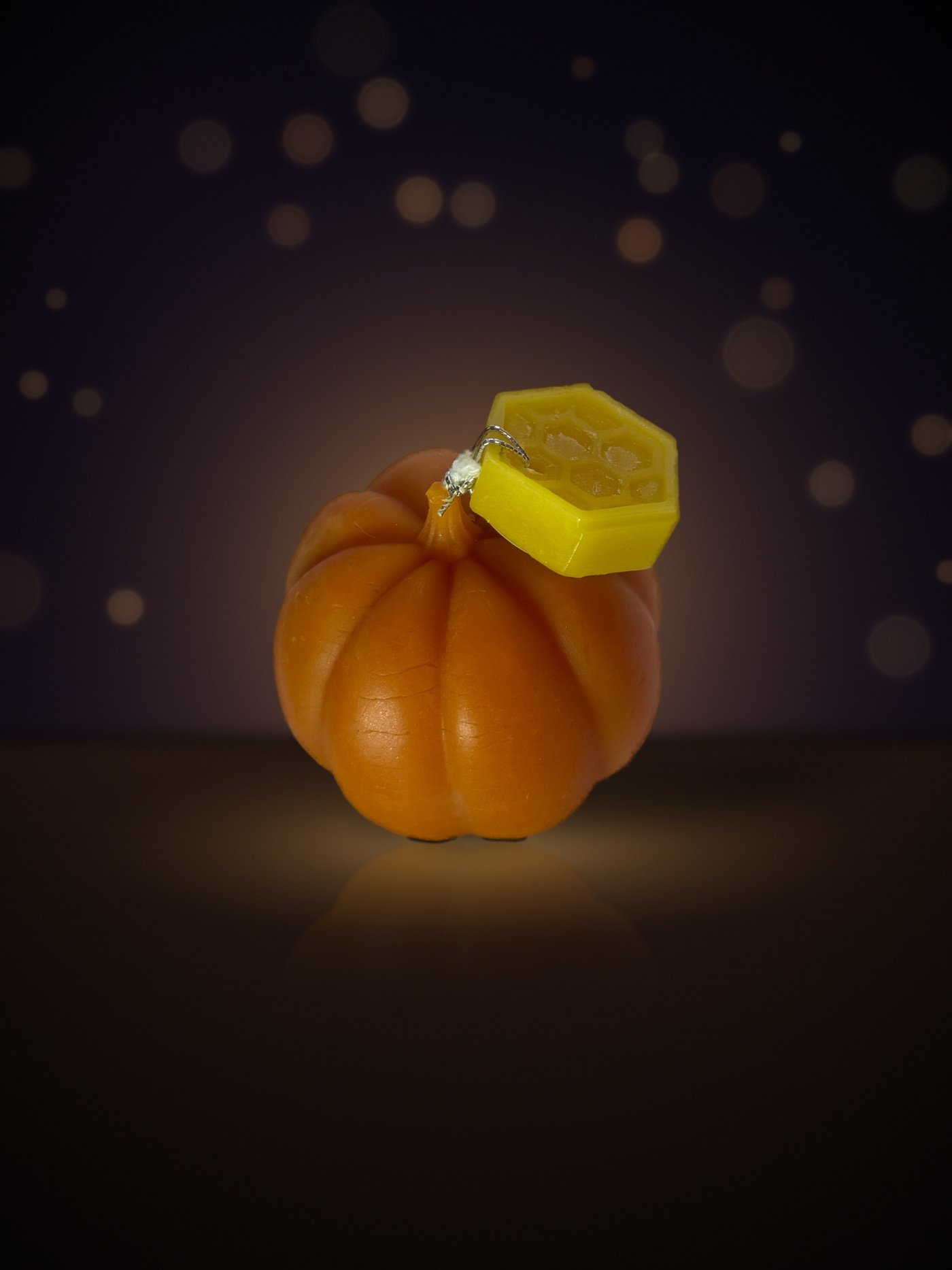 Maine beeswax pumpkin candle, small round shape, orange, with honeycomb tag, warm candlelit background