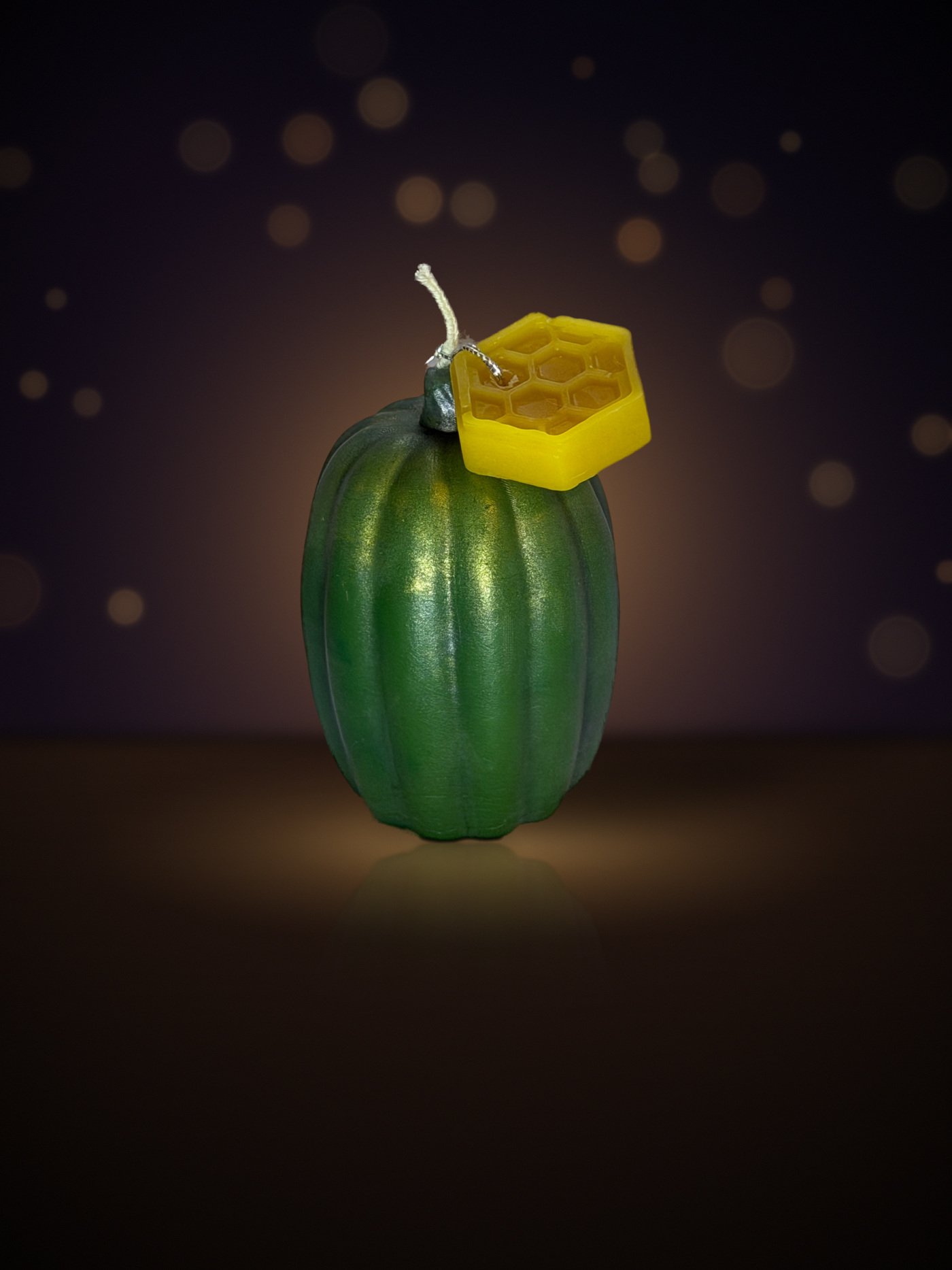 Maine beeswax pumpkin candle, tall shape, green, with honeycomb tag, warm candlelit background