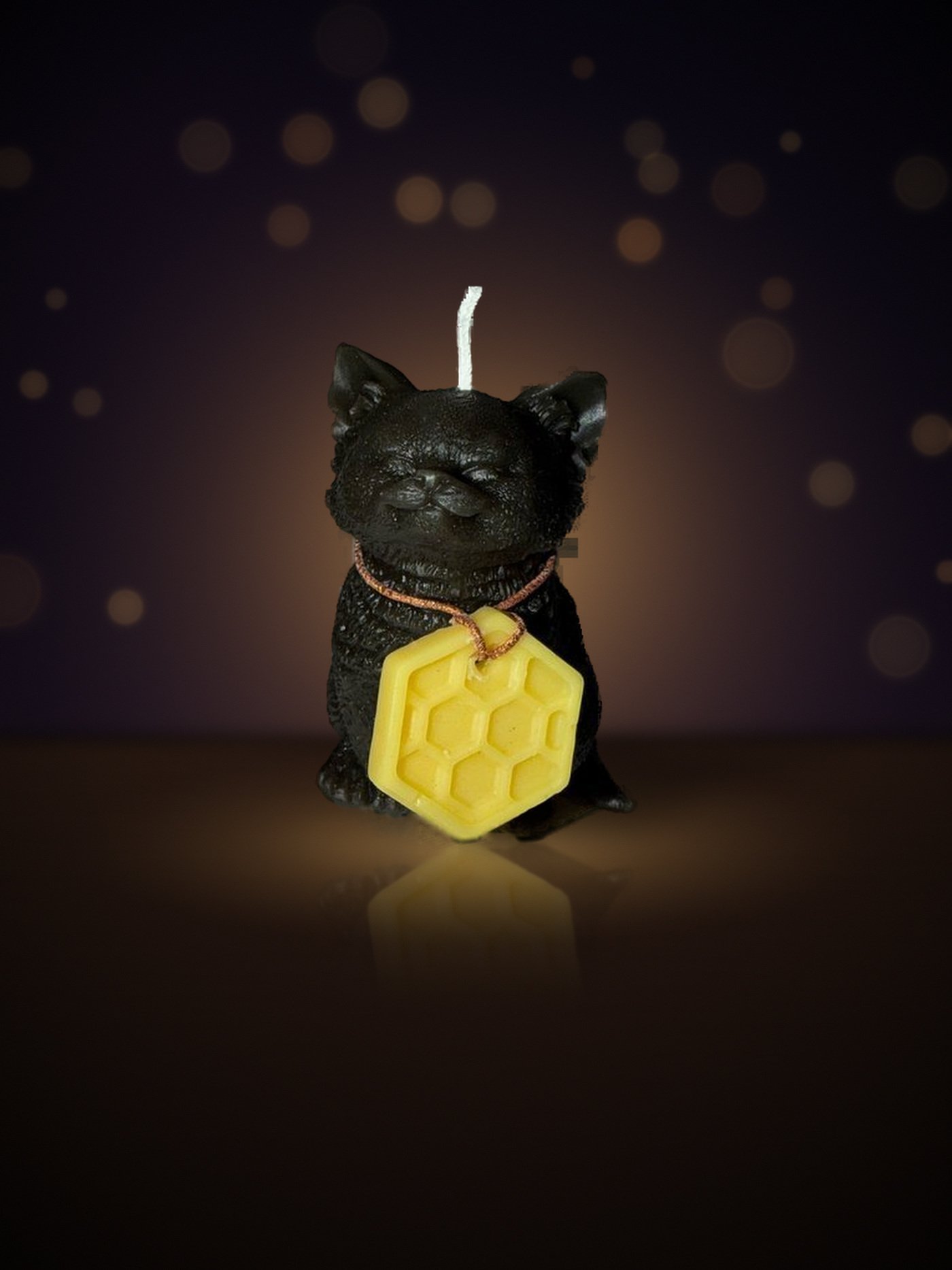 Maine beeswax RBF resting-face cat candle in matte black with honeycomb tag, warm candlelit background