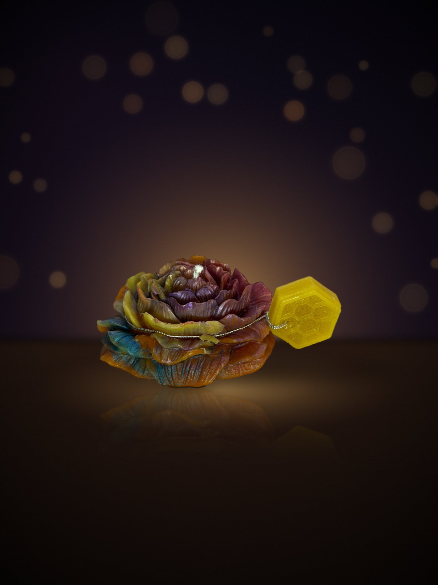 Maine beeswax rose candle in amber, blue and purple with honeycomb tag, warm candlelit background