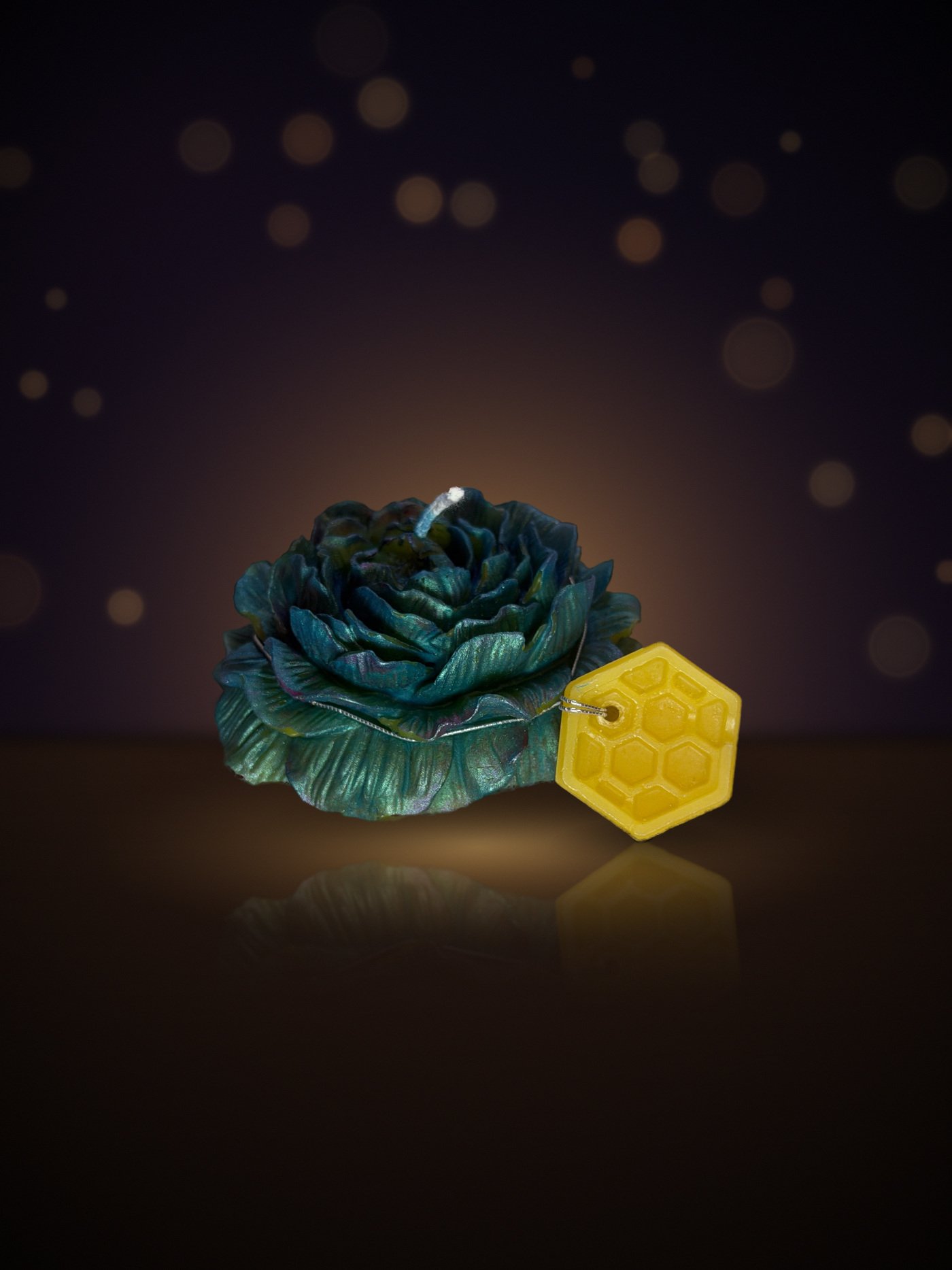 Maine beeswax rose candle in deep teal with honeycomb tag, warm candlelit background