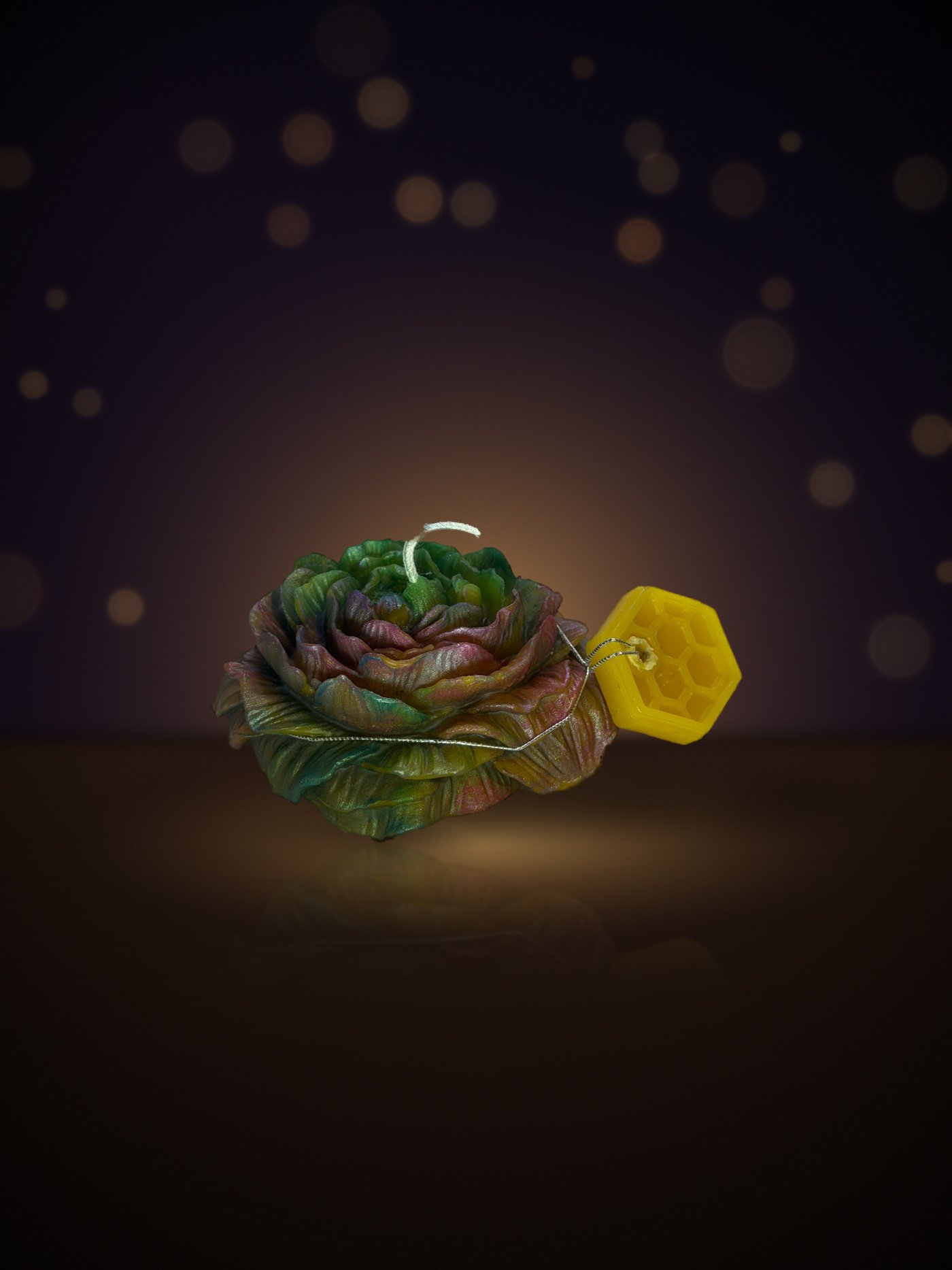 Maine beeswax rose candle in green and pink with honeycomb tag, warm candlelit background