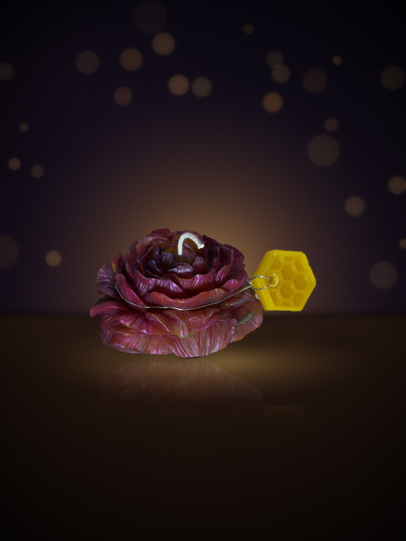 Maine beeswax rose candle in magenta with honeycomb tag, warm candlelit background