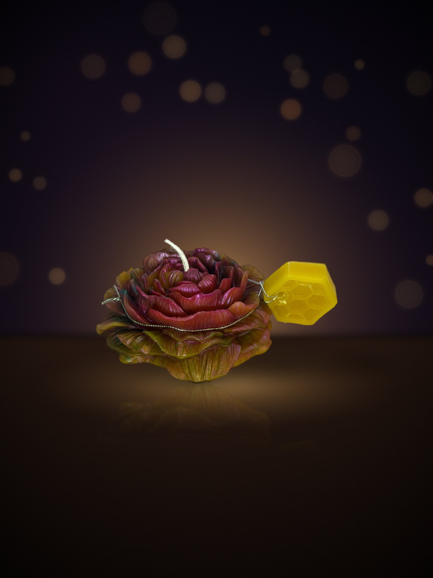 Maine beeswax rose candle in magenta and olive with honeycomb tag, warm candlelit background