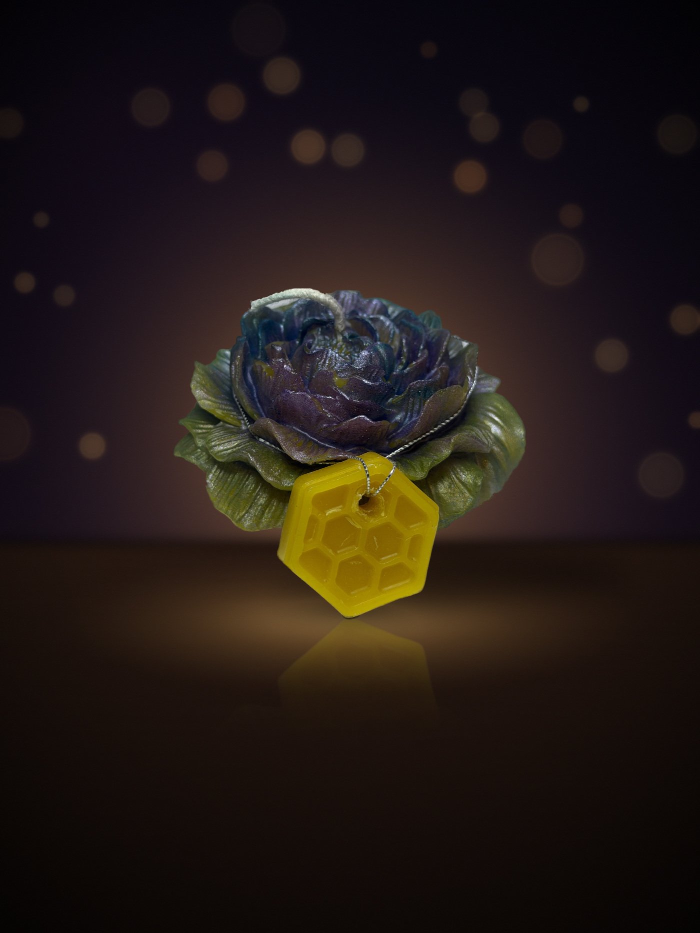 Maine beeswax rose candle in purple with green leaves with honeycomb tag, warm candlelit background