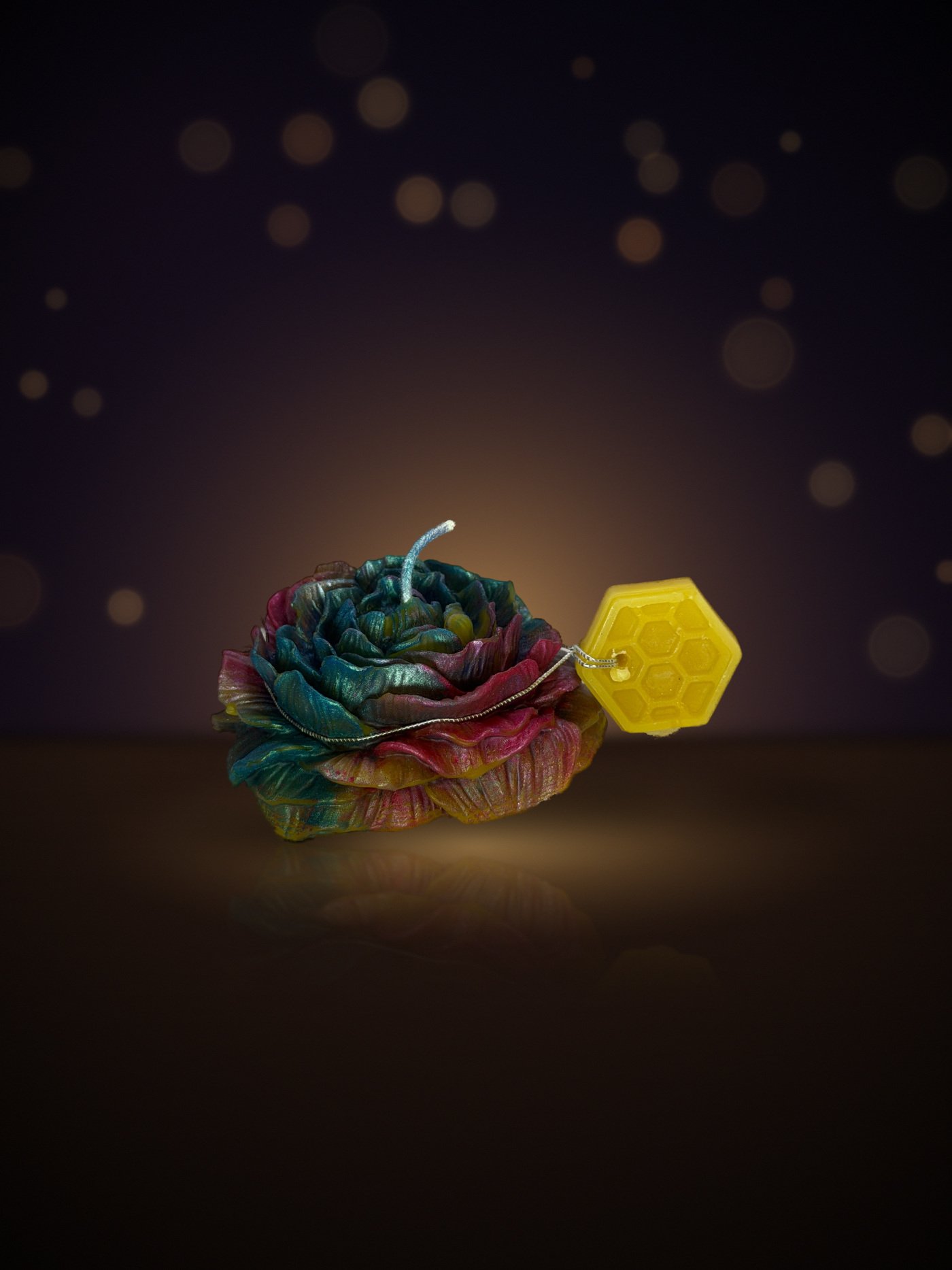 Maine beeswax rose candle in rainbow teal and pink with honeycomb tag, warm candlelit background