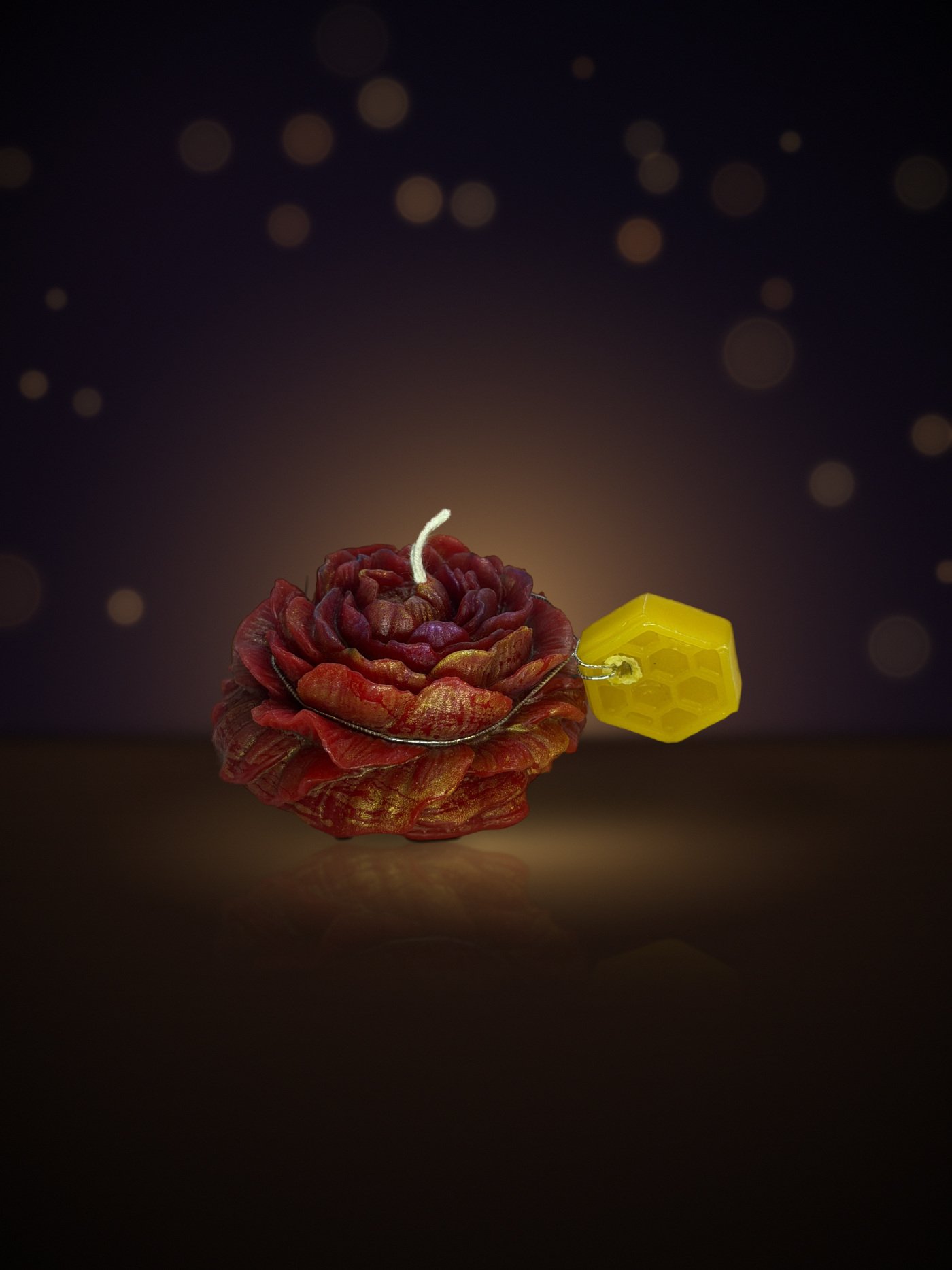 Maine beeswax rose candle in red and gold with honeycomb tag, warm candlelit background