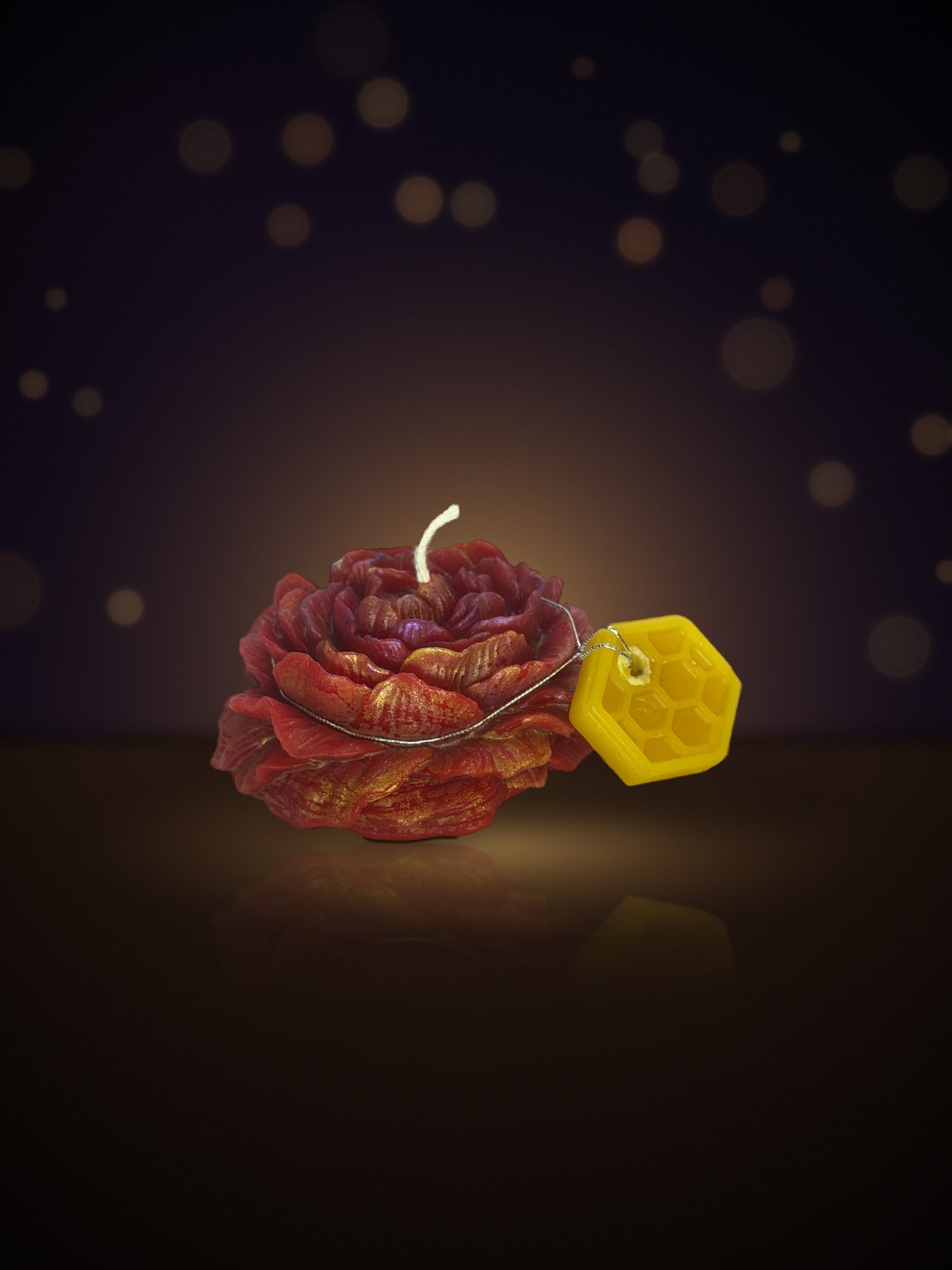 Maine beeswax rose candle in red and gold, close-up with honeycomb tag, warm candlelit background