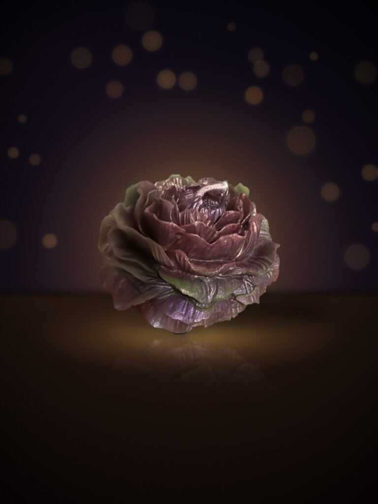 Maine beeswax rose candle in burgundy and mauve with sage-green petal tips, warm candlelit background