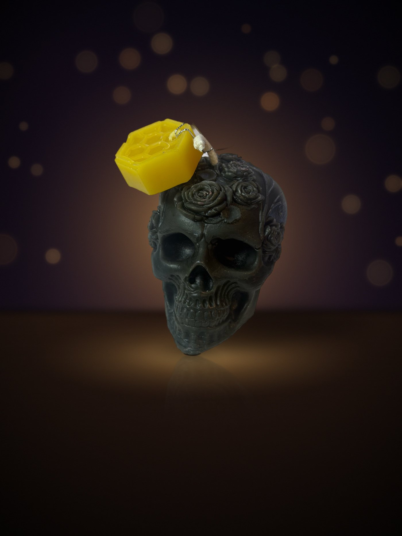 Maine beeswax skull candle crowned with roses, black, with honeycomb tag, warm candlelit background