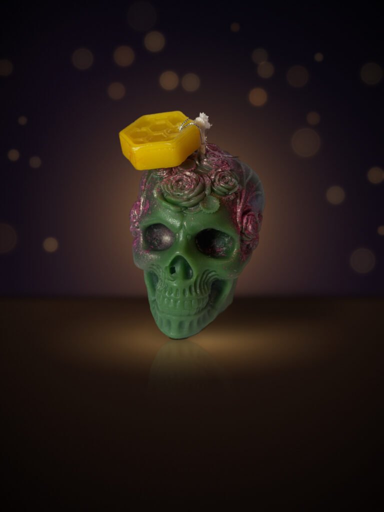 Maine beeswax skull candle crowned with roses, green with magenta roses, with honeycomb tag, warm candlelit background