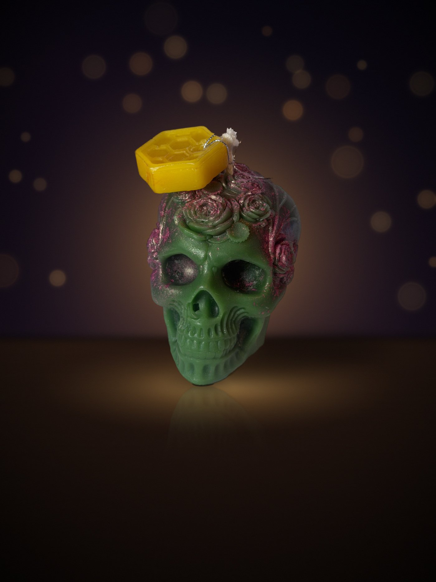 Maine beeswax skull candle crowned with roses, green with magenta roses, with honeycomb tag, warm candlelit background