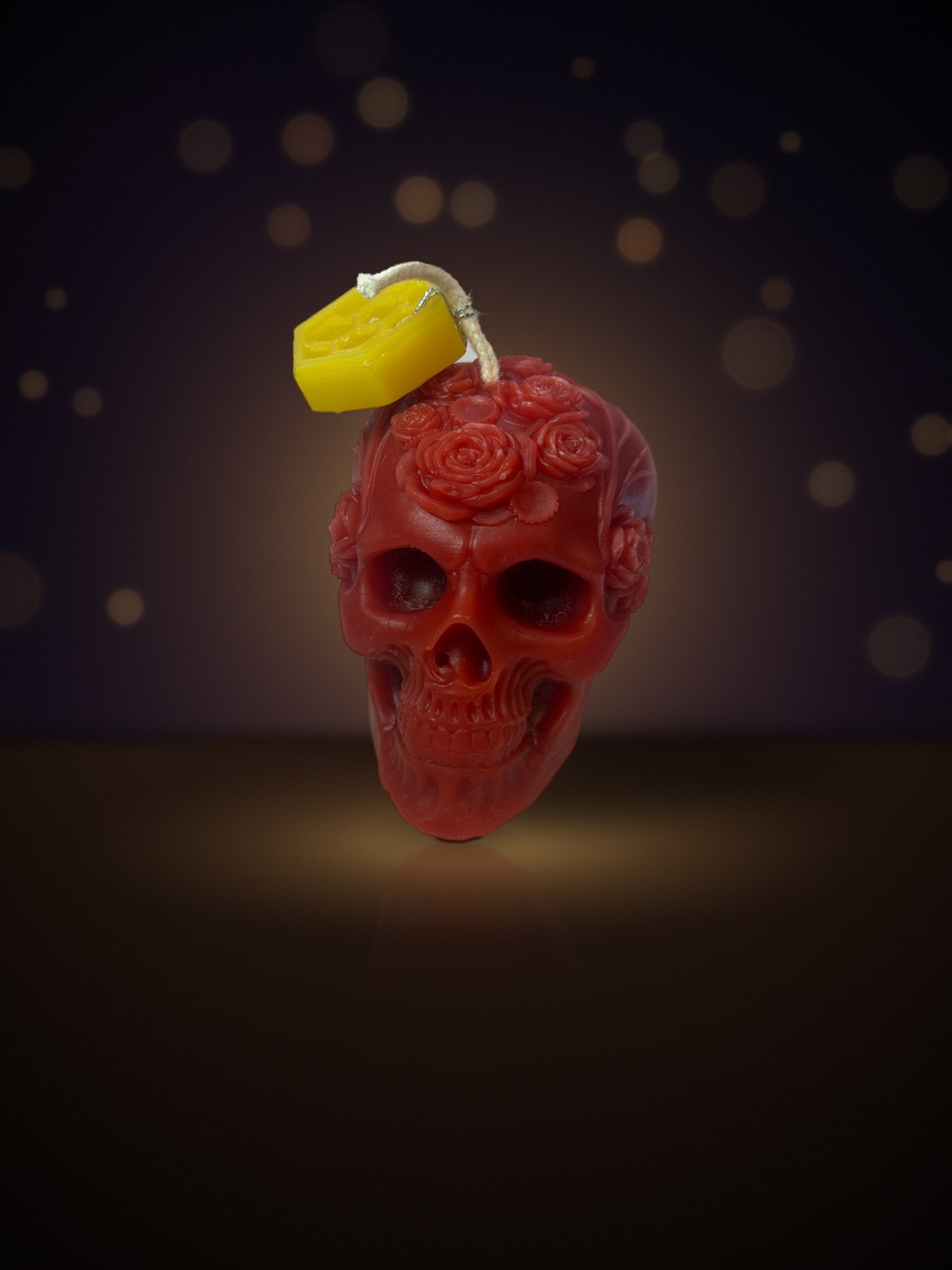 Maine beeswax skull candle crowned with roses, red, with honeycomb tag, warm candlelit background