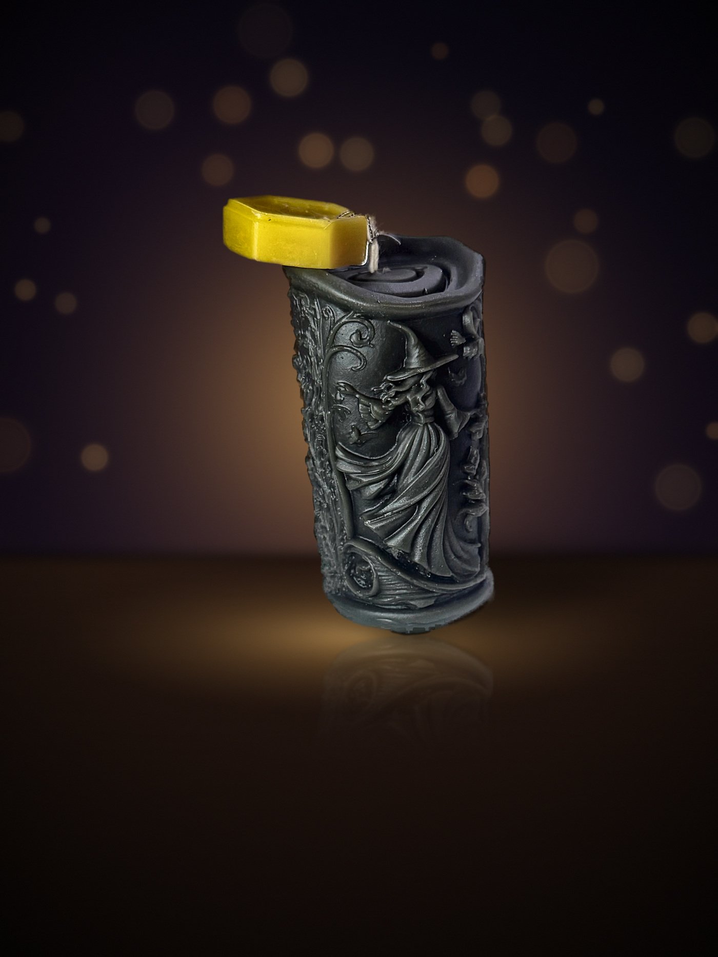 Maine beeswax witch pillar candle in black with a witch relief and honeycomb tag, warm candlelit background