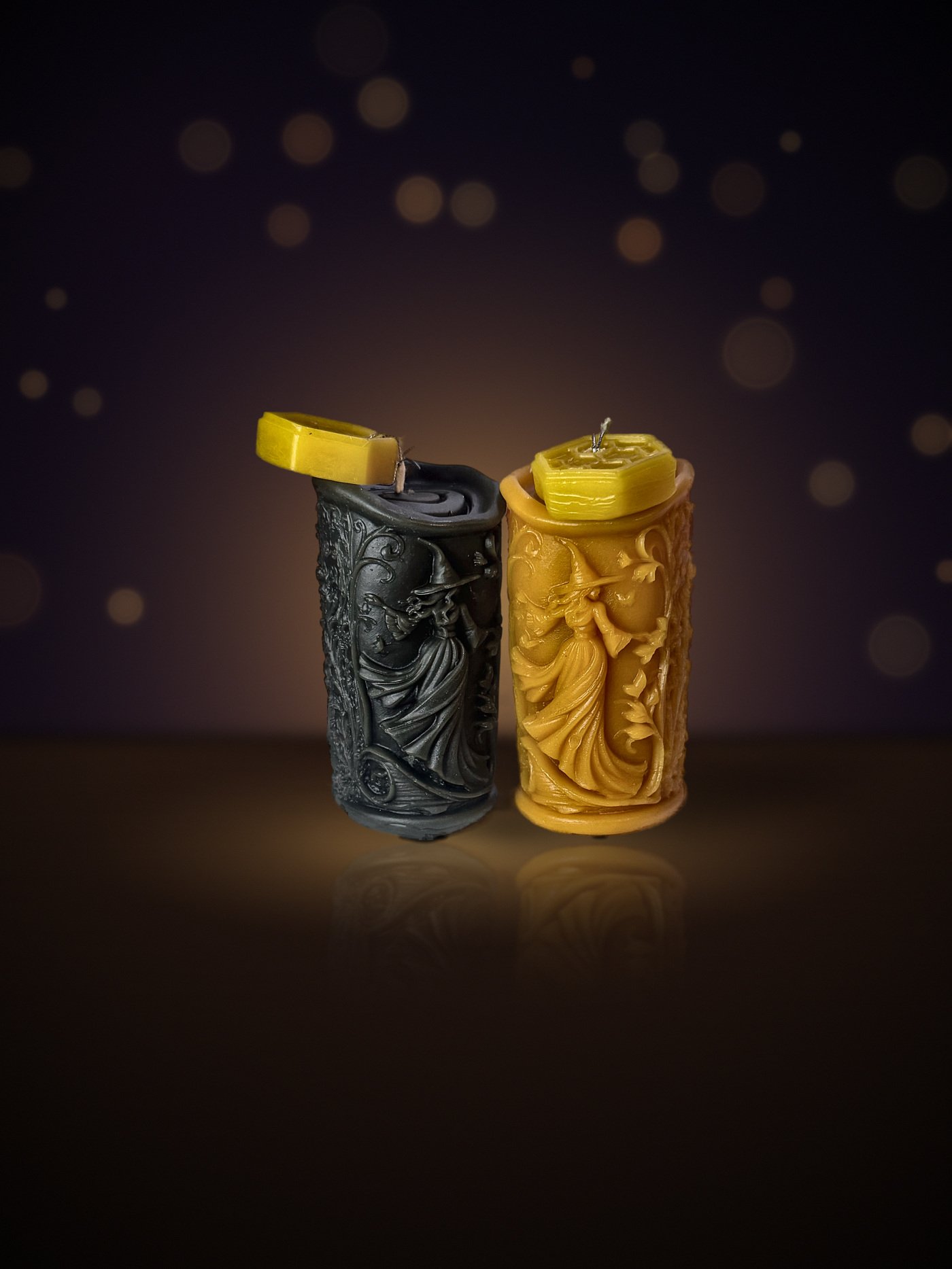 Two Maine beeswax witch pillar candles, black and natural beeswax gold, each with a honeycomb tag, warm candlelit background
