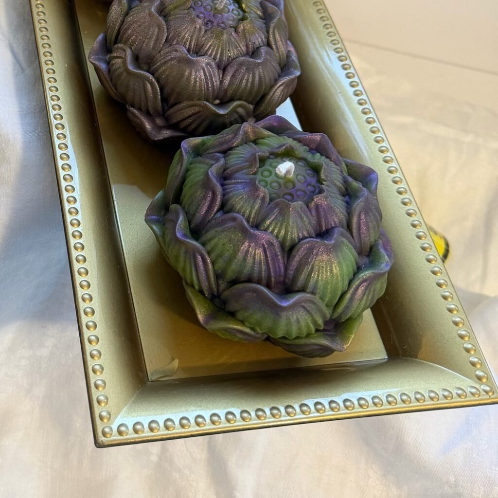 Two unwrapped Conway Candle Sanctuary beeswax artichoke candles with purple and green mica on a gold beaded tray